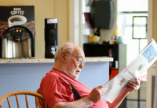 Older man reading a newspaper while sitting at a table.