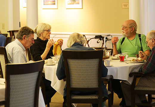 Group of seniors talking and eating dinner around a large circular table.